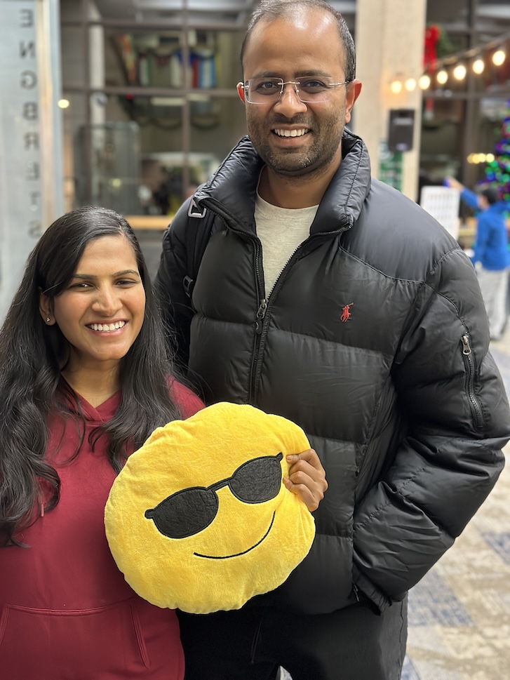 People smiling at camera holding an emoji pillow